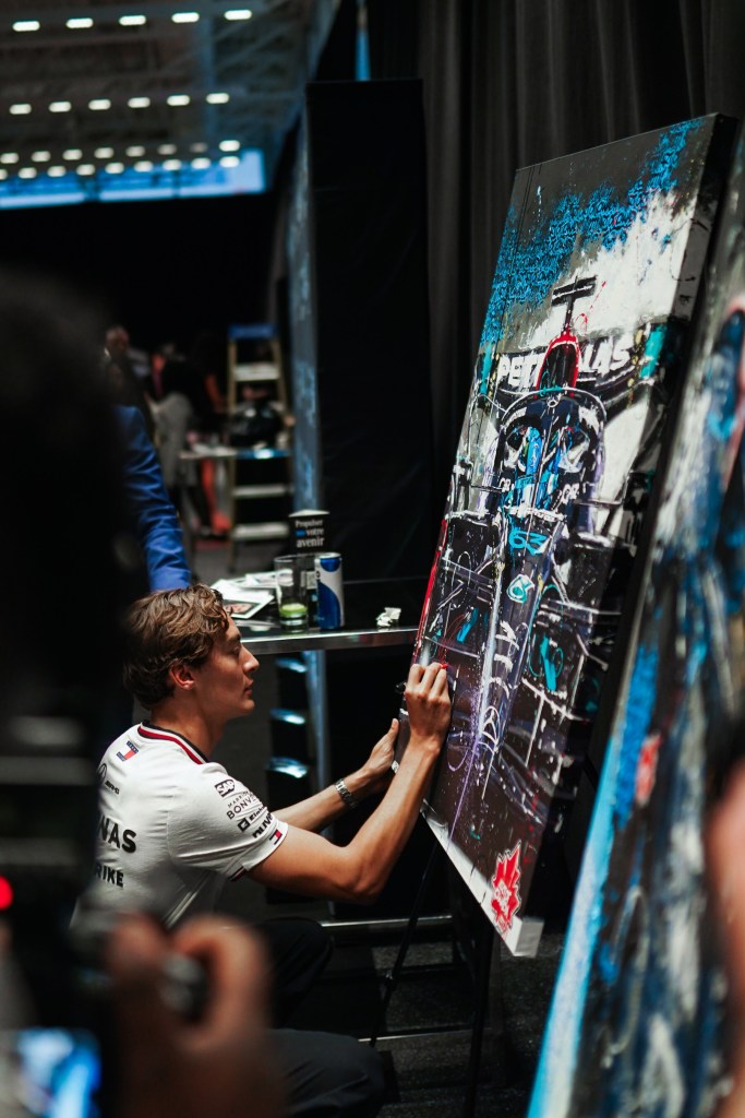 George Russell signing a piece of art