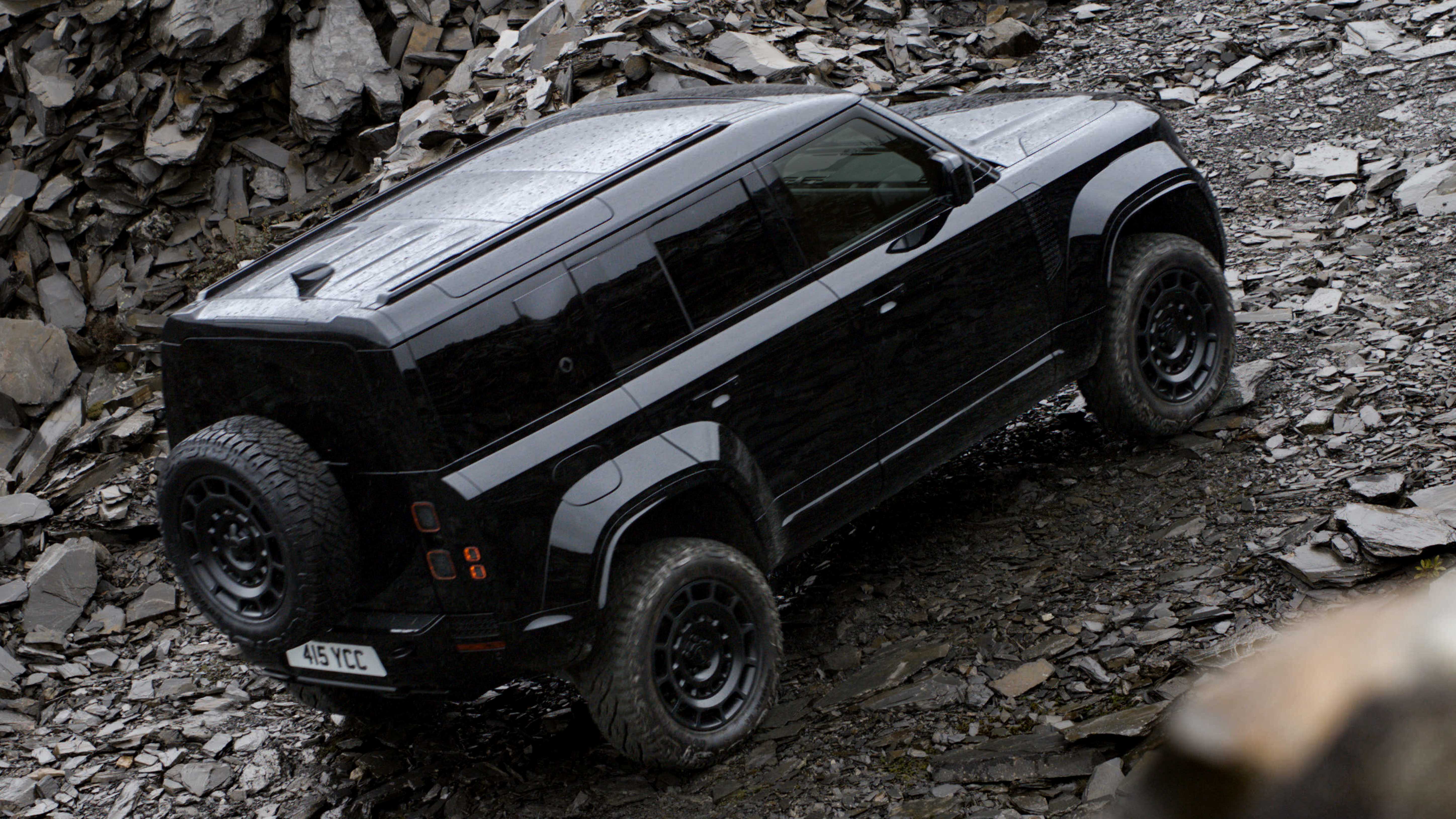2026 Land Rover Defender OCTA Black driving up a rocky hill