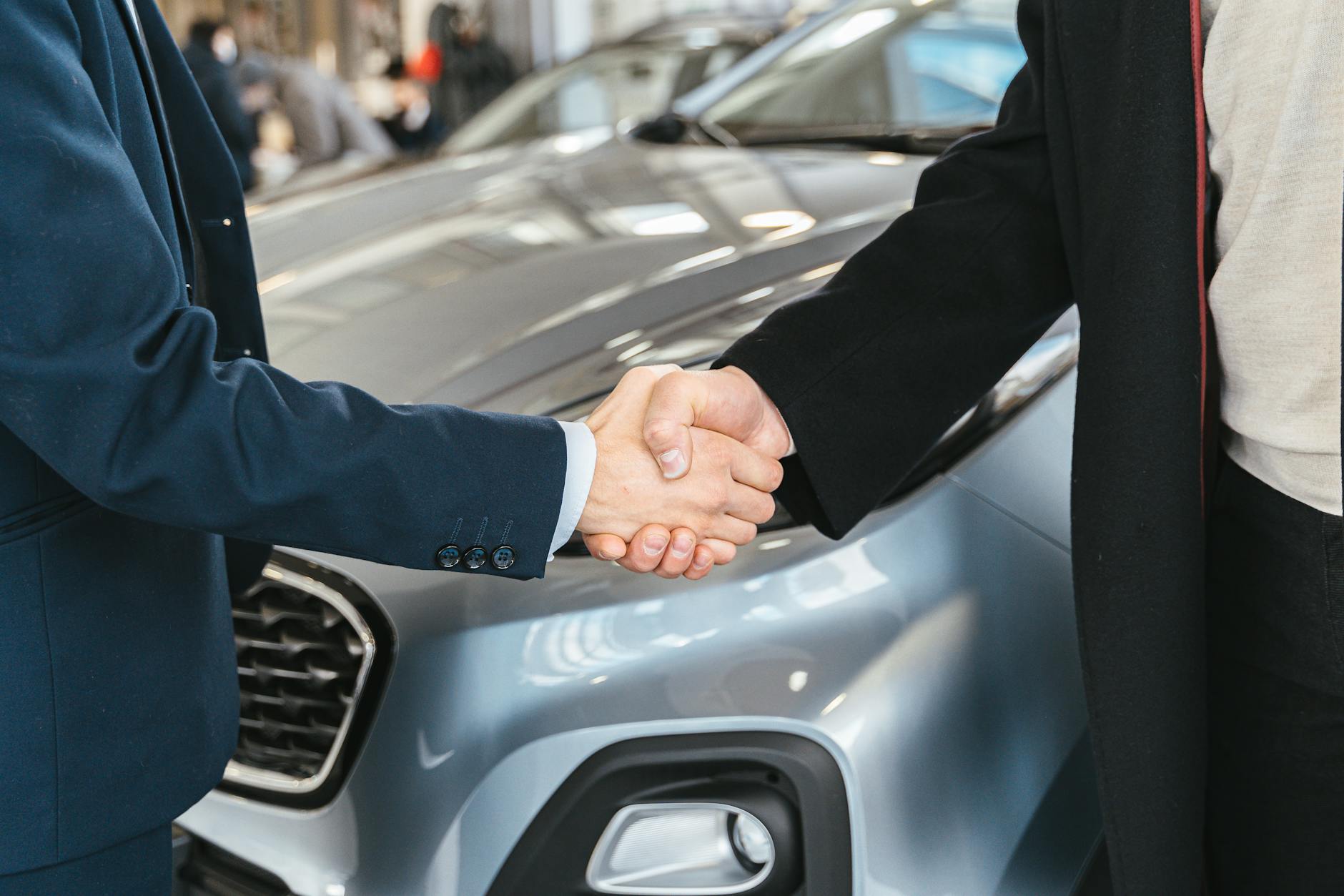 Two men shaking hands in front of car