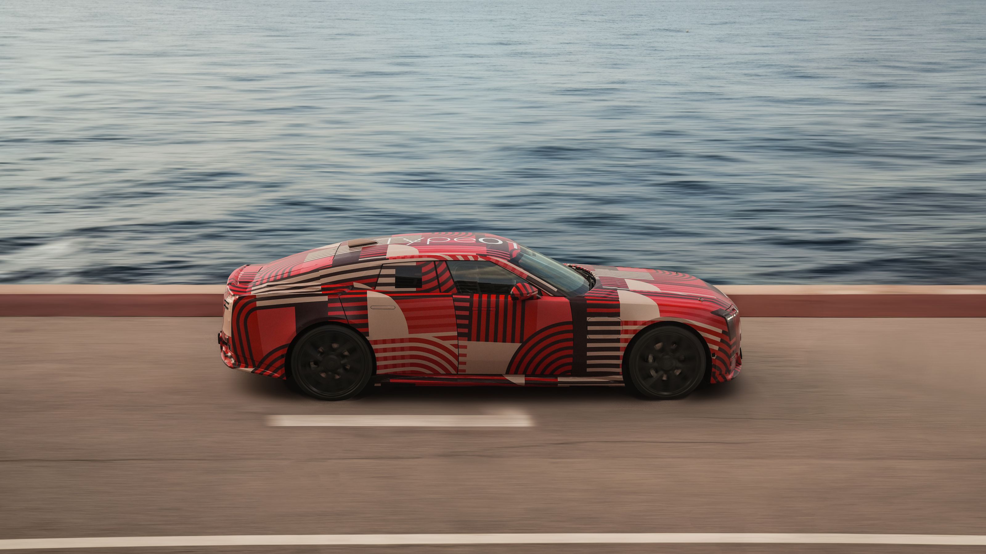 Camouflaged Jaguar Type 01 prototype driving along Monaco shoreline