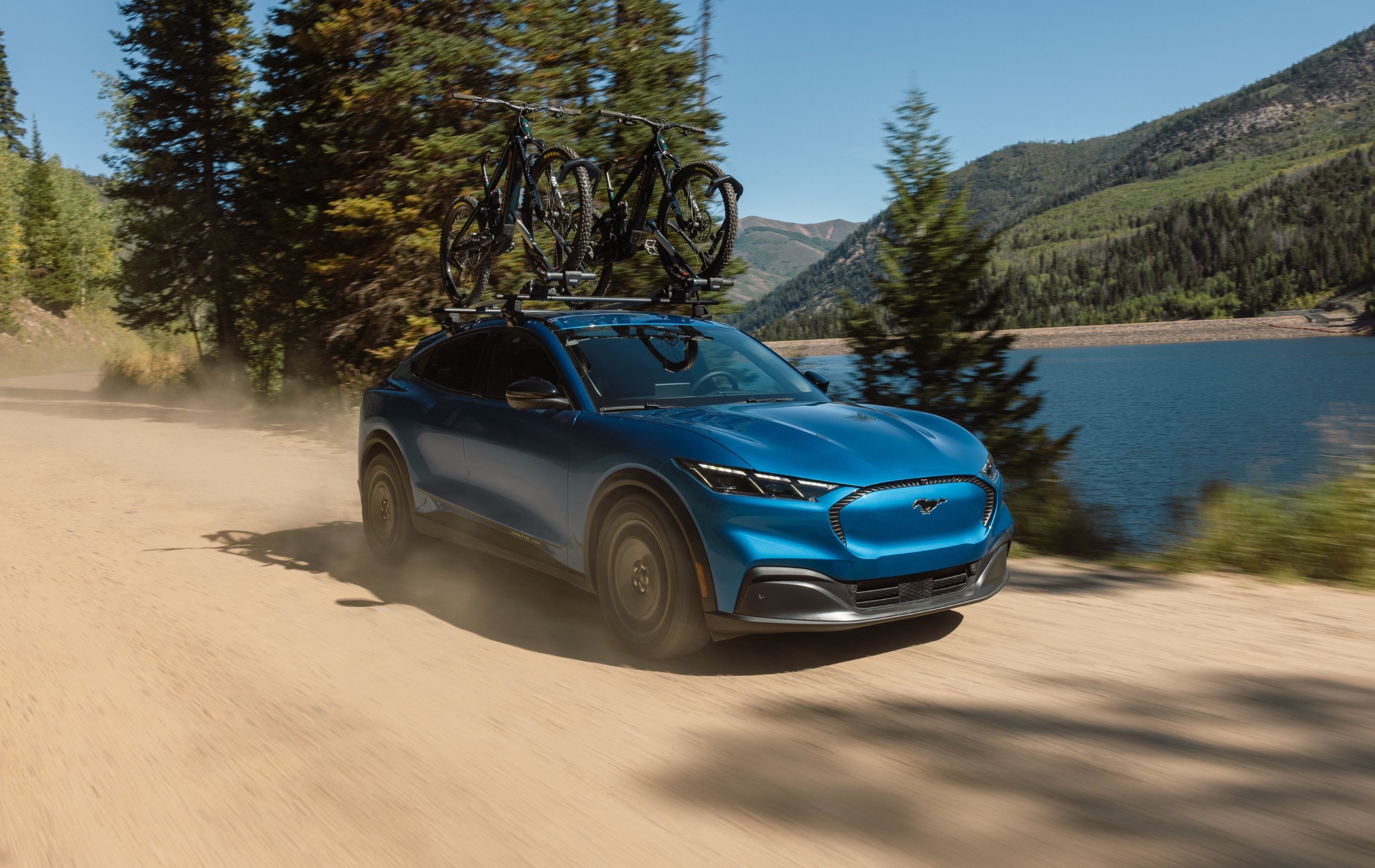 2027 Ford Mustang Mach-E Trail with bikes on roof driving on sand road
